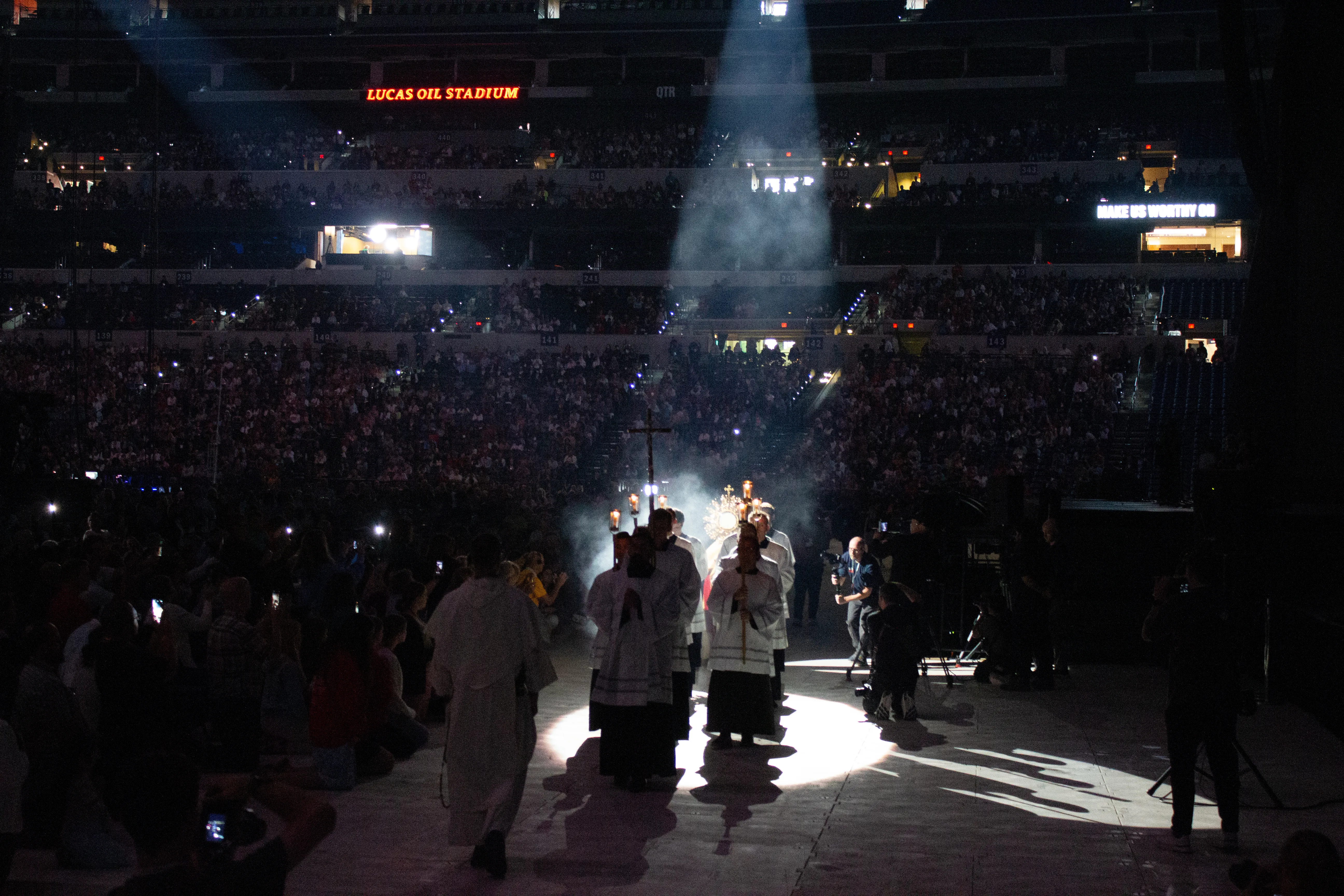 Father Boniface Hicks, OSB, a sought-after spiritual director and retreat master, processes the massive golden monstrance containing the Eucharist into the midst of the assembled crowd in Lucas Oil Stadium. | Photo by Jonah McKeown/CNA.