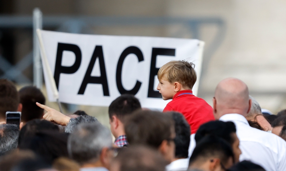 A child is near a sign that says "Pace," peace in Italian, as visitors gather to pray the Angelus with Pope Francis in St. Peter’s Square at the Vatican