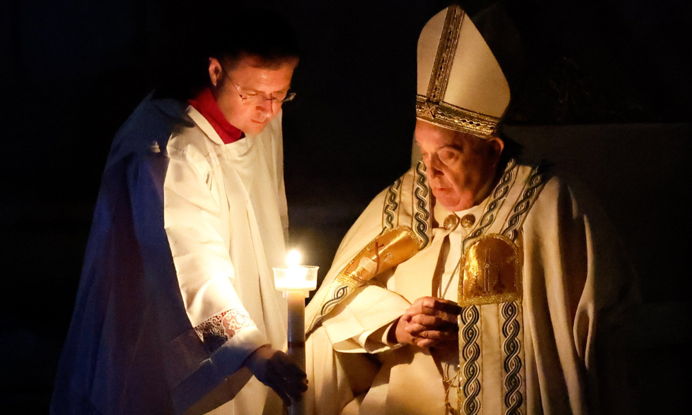 An aide hands Pope Francis his candle, lighted from the paschal candle, at the beginning of the Easter Vigil Mass in St. Peter's Basilica at the Vatican March 30, 2024.