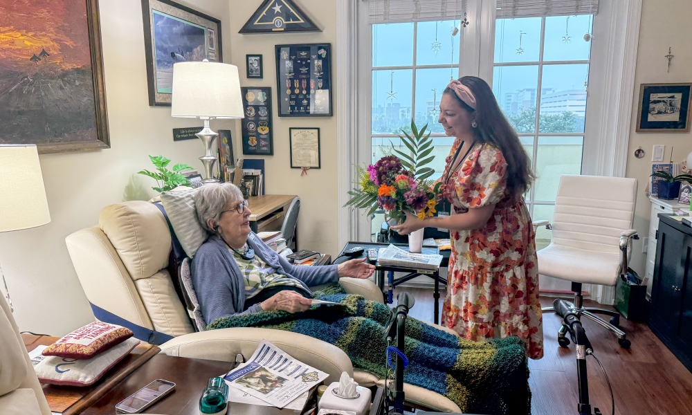 A woman delivers flowers and a spiritual bouquet card to a homebound parishioner.