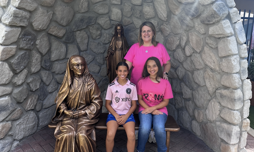 Students from Mother Teresa of Calcutta Catholic School dressed in pink sitting next to a statue of Mother Teresa.