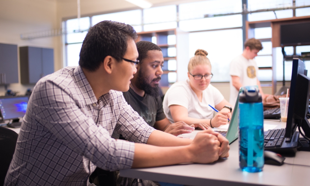 Dr. Van Nguyen of the College of Computing, Artificial Intelligence, Robotics, and Data Science (CARDS) works with Saint Leo computer science-cybersecurity students.