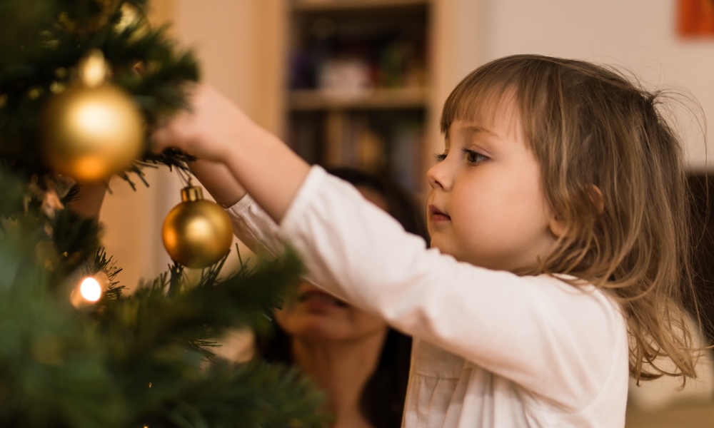 Little girl hangs ornament on a tree